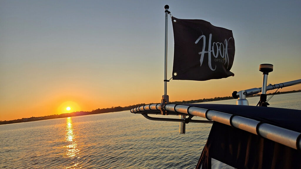 Sunset over water with a flag on a boat railing, featuring the word 'Hook'