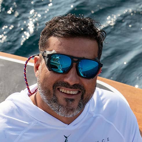 Man smiling into camera wearing hook optics 305 glacier sunglasses with water in the background.