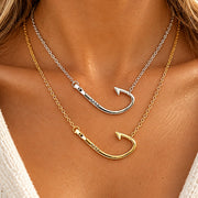 Two layered fishhook necklaces on a model's neck, one in silver and one in gold, both engraved with the name 'MIA'.