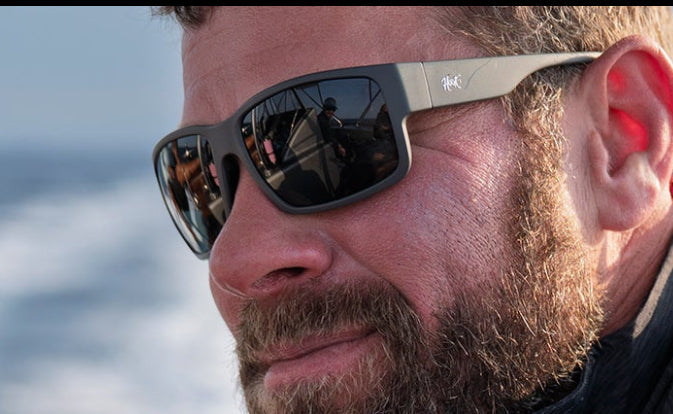 Man wearing amazing sunglasses and a black jacket on a boat with water in the background