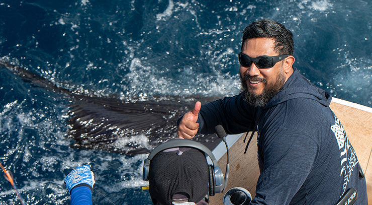 Two happy anglers on a boat with one holding a large fish, smiling and giving a thumbs-up wearing hook optics